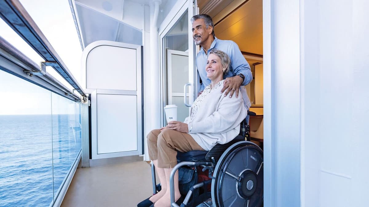 Man with arm around woman in wheelchair on balcony of a cruise ship.
